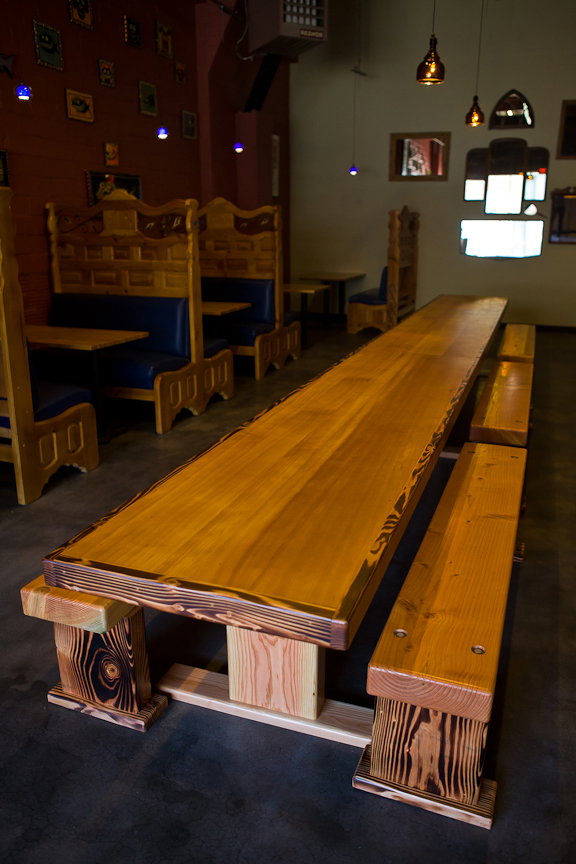 Other menu items mentioned include Belgian frites with housemade dipping sauces and haluski, a Czech noodle dish. This 21-foot communal table is made from reclaimed wood.